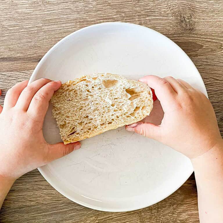 Child holding a piece of soft sourdough bread on a white plate.