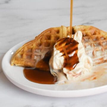 crispy sourdough waffles without milk with ice cream and maple syrup pouring over them on a plate