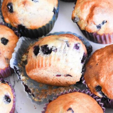Sourdough discard blueberry muffin on a marble surface, circled by other muffins.