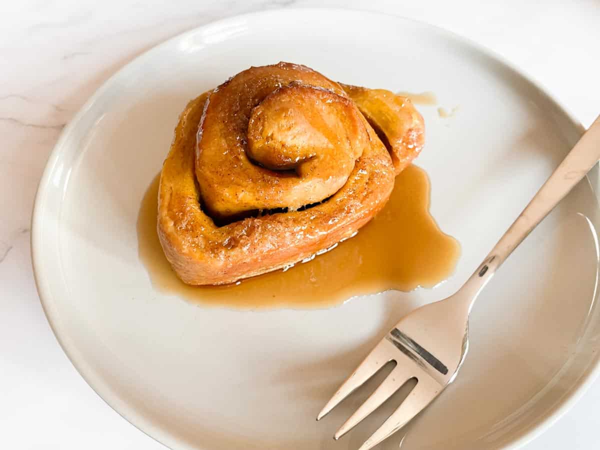 Sourdough pumpkin cinnamon roll served on a plate with a little fork.