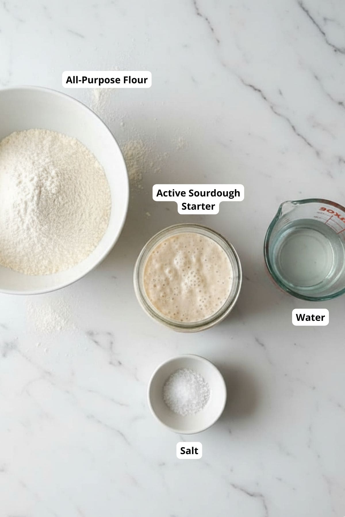 Ingredients for long fermented sourdough bread arranged on a surface, including flour, water, salt, and sourdough starter.