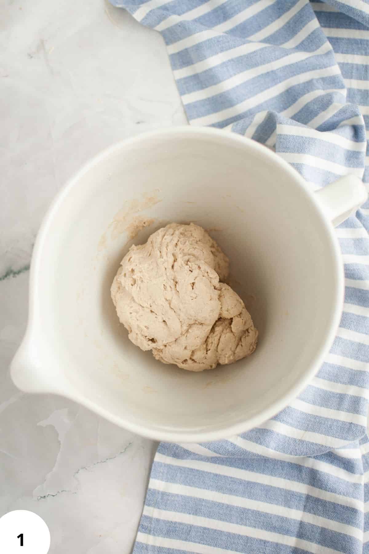 Sourdough bread dough during stretch and fold process in a white mixing bowl.