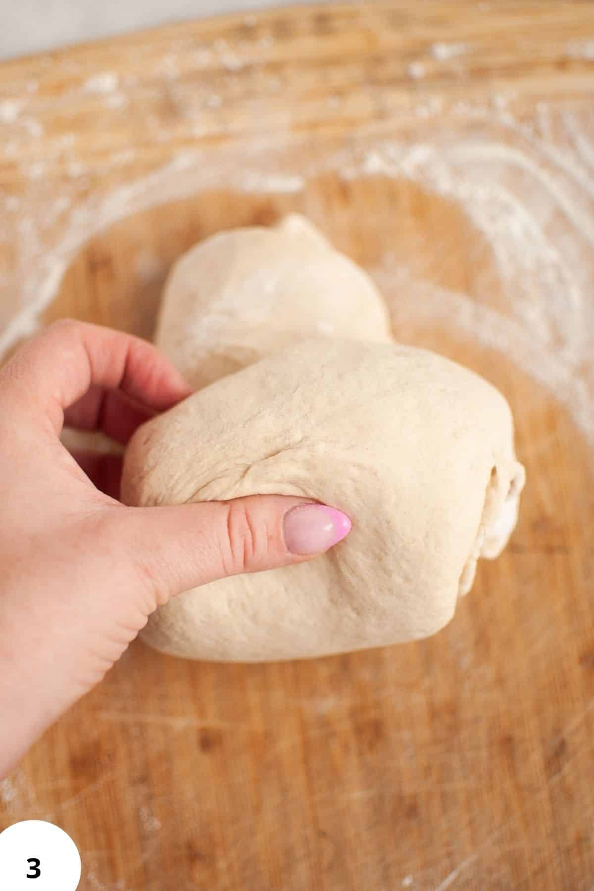 Hand performing stretch and folds on sourdough dough on a wooden surface.