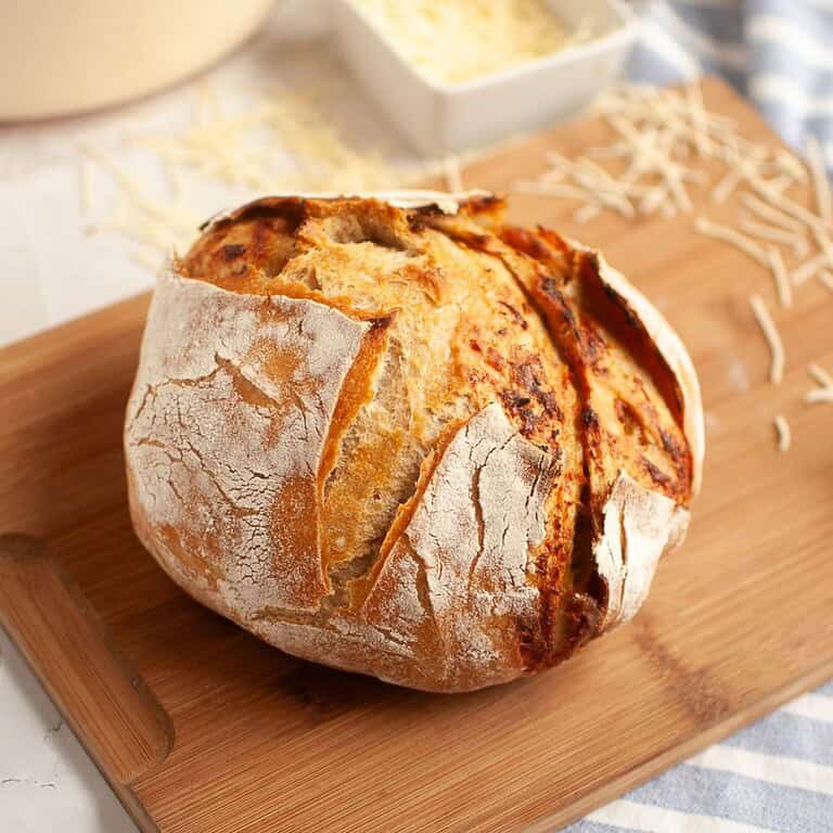 Fresh sourdough bread with roasted garlic and Parmesan cheese on a wooden board.