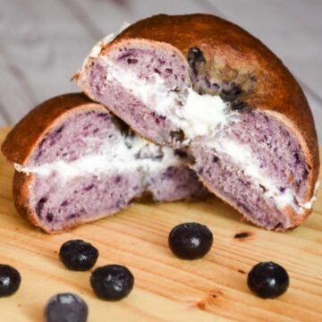 Sourdough Blueberry bagel sandwich cut in half, greek yogurt in the middle, on a round wooden board.