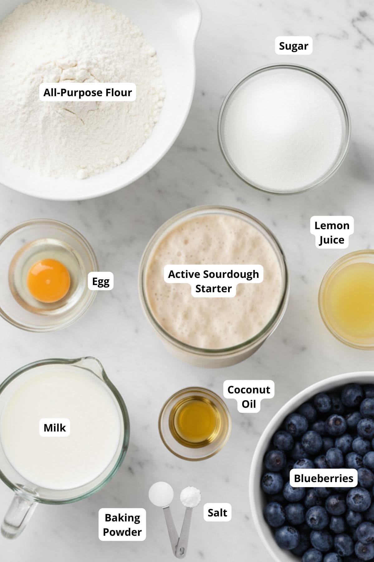 Ingredients for making a sourdough discard blueberry and lemon quick bread arranged in a marble surface.