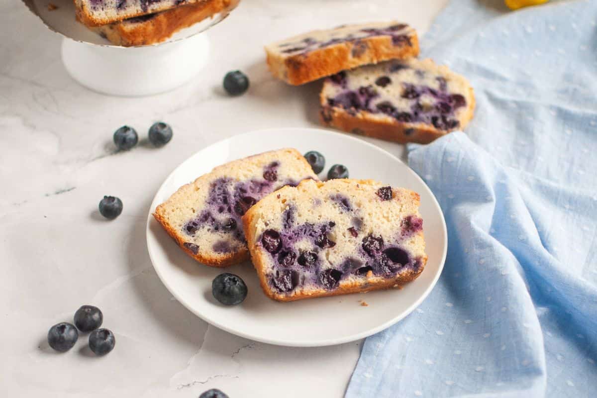 Sourdough discard blueberry lemon quick bread with fresh blueberries on a white plate.