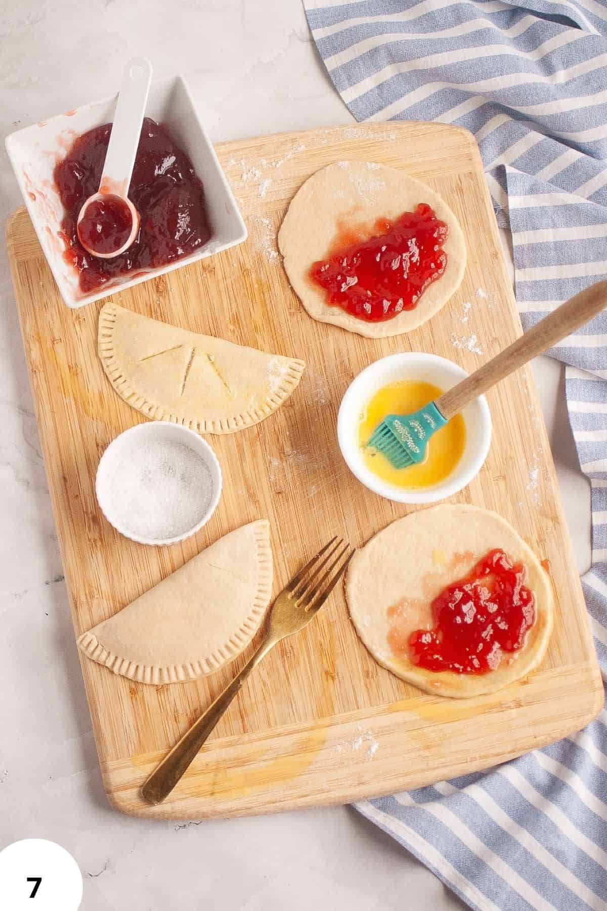 Sourdough dough with jam filling and folding tools on wooden board.