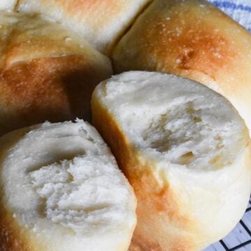 Sourdough rolls on a cooling rack, two of them separated to show a soft interior.