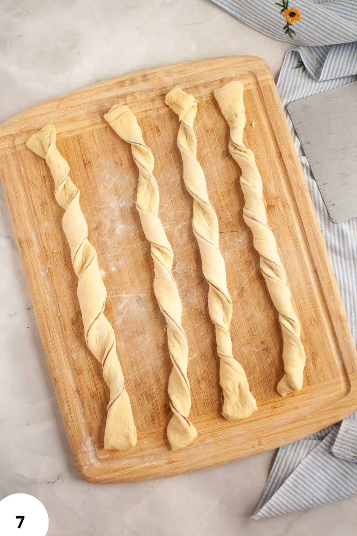 Four twisted sourdough dough strands on a wooden board for baking.