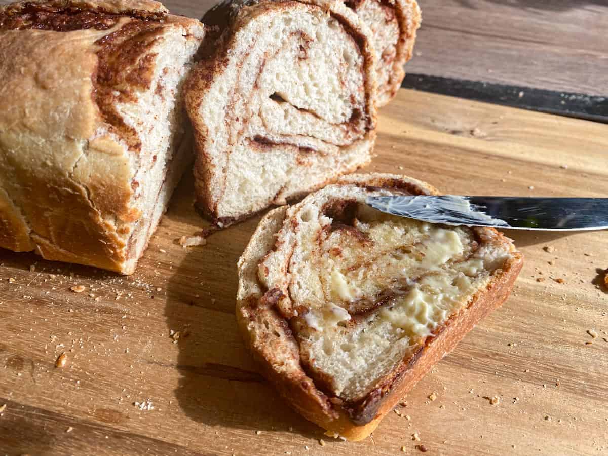 Sourdough cinnamon sugar bread with some slices cut off on a wooden cutting board.