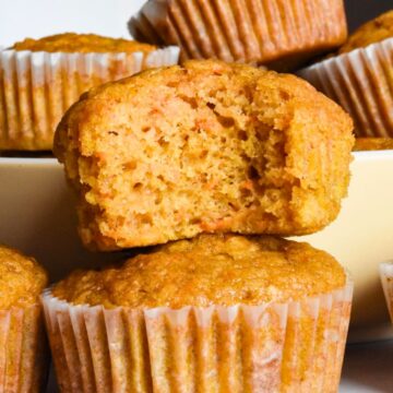 Sourdough carrot cake muffins stacked on top of each other with one with a bite out of it.