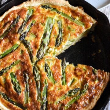 A sourdough quiche in a sourdough pie crust baked in a large cast iron skillet and topped with asparagus.
