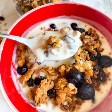 A bowl of granola with yogurt, with a silver spoon taking a spoonful.