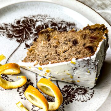 A piece of frosted cake on a silver plate with oranges on top.