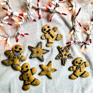 Decorated sourdough gingerbread cookies on a kitchen towel with some Christmas lights.