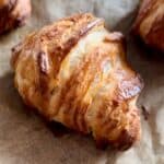 Close-up of a golden, flaky croissant resting on parchment paper.