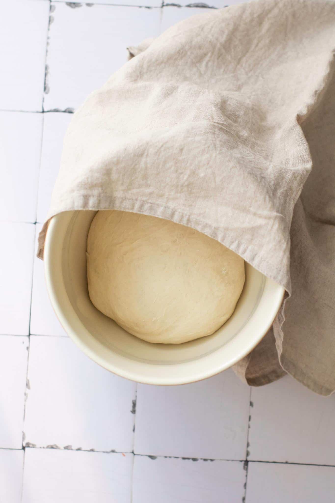 Dough in a bowl slightly covered with cloth.