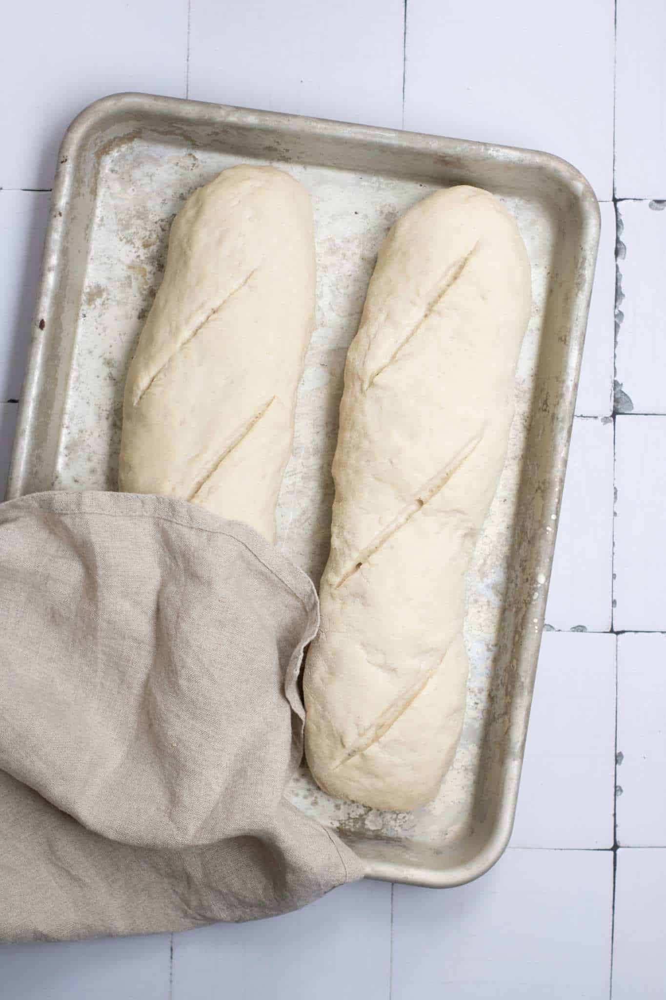 Two dough placed in a baking tray in a rectangle shape slightly covered with cloth.