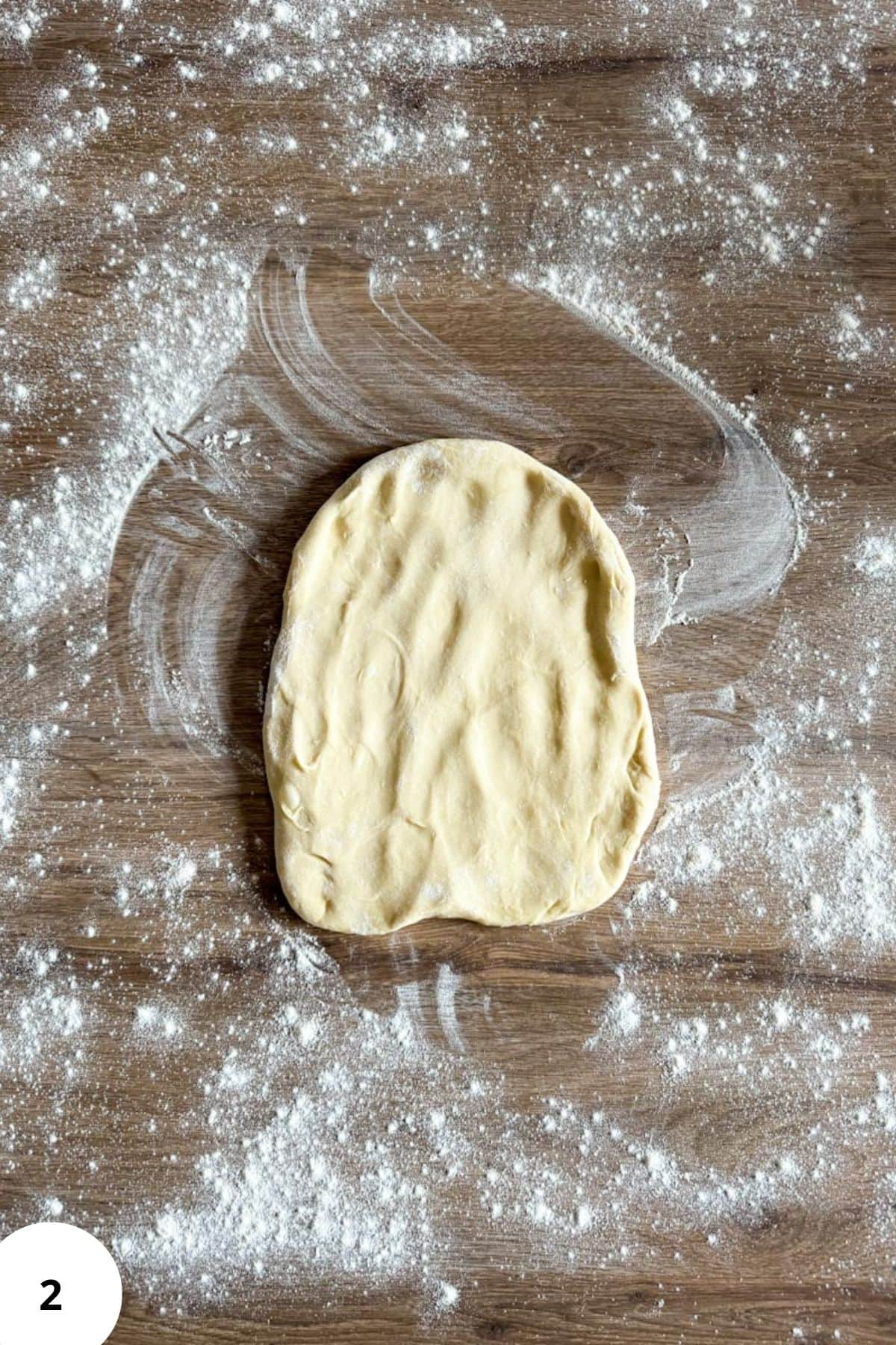 Flattened dough resting on a floured rustic surface.