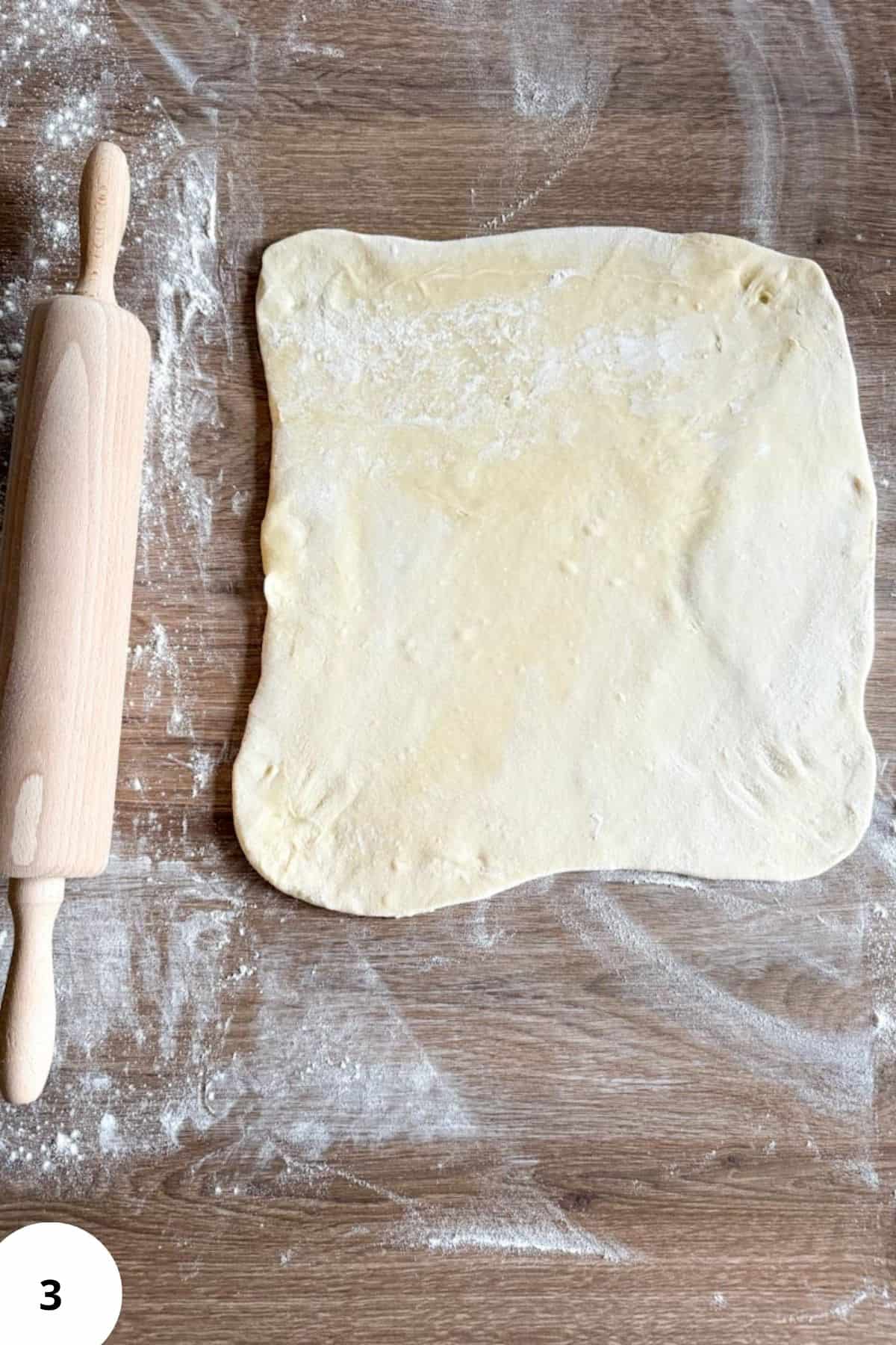 Flattened dough resting on a rustic surface with a rolling pin nearby.