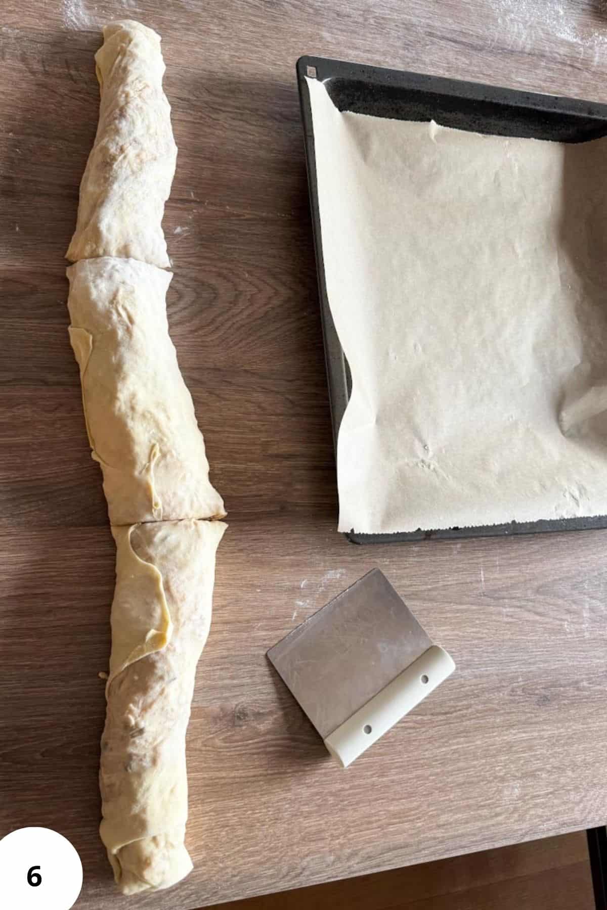 A divided roll of apple strudel on the table next to cookie sheet.
