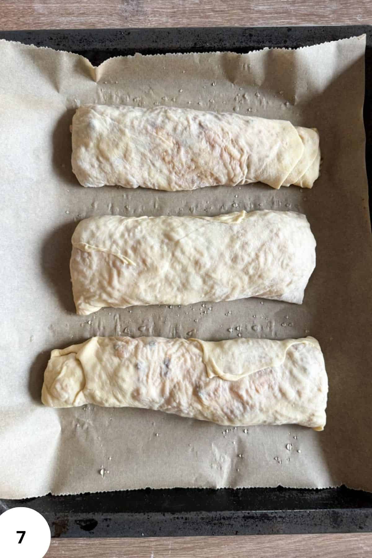 Unbaked apple strudel rolls on a cookie sheet.