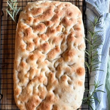 Sourdough focaccia bread on a black wire rack with rosemary as a decoration.