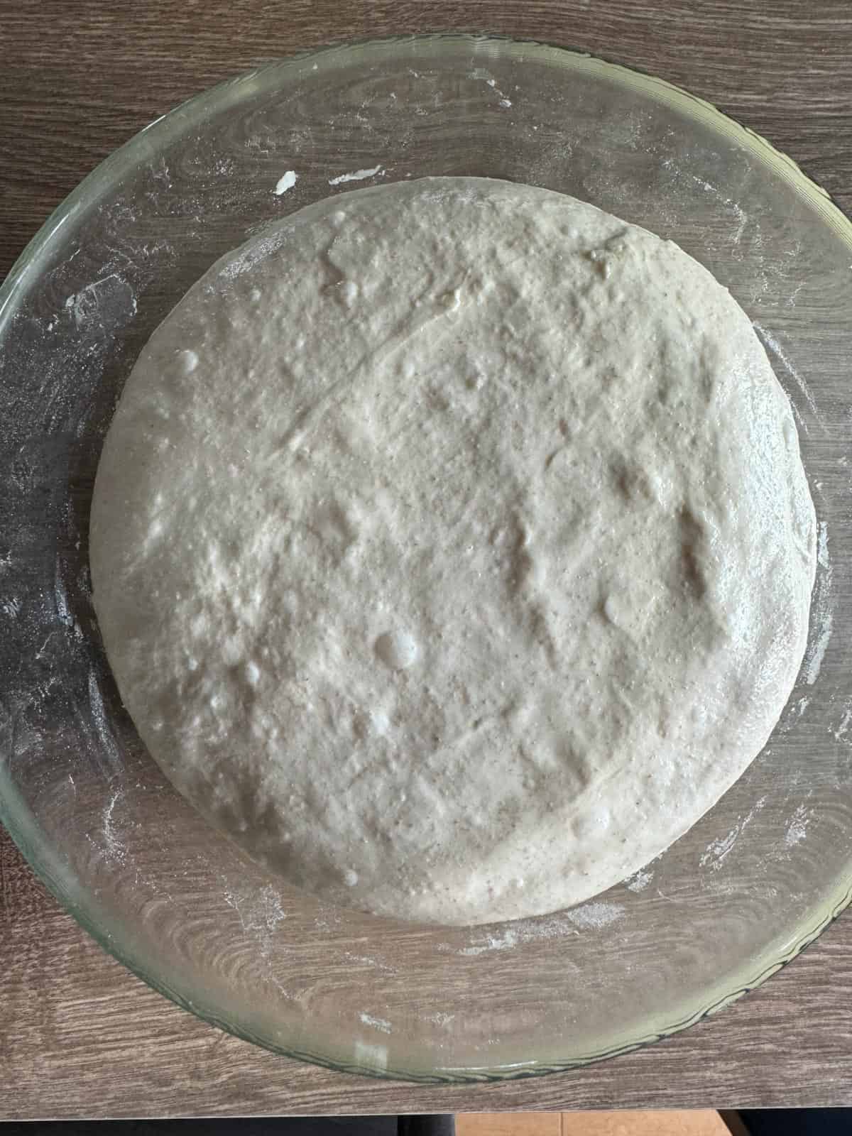 Bread dough fermenting in a glass bowl.