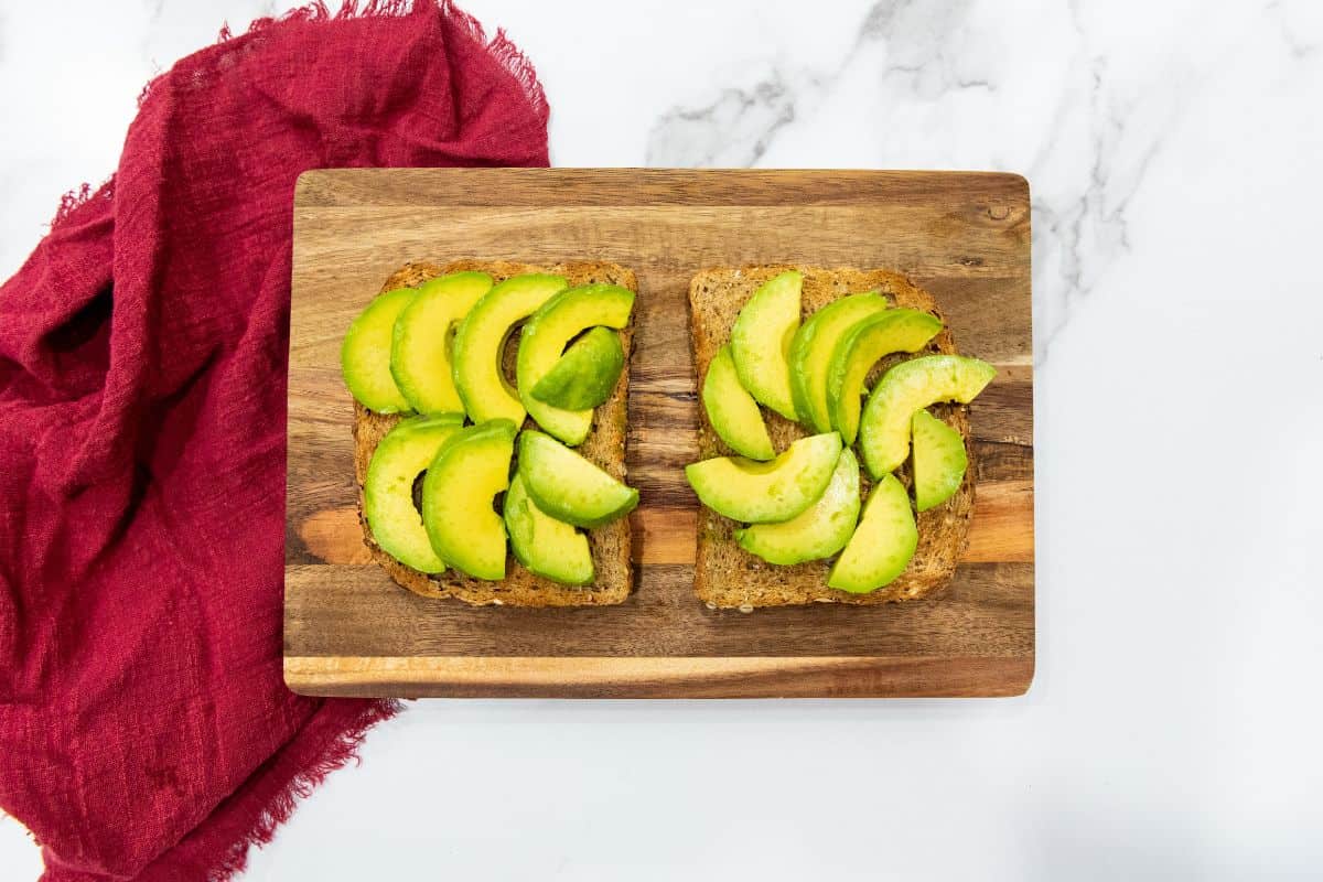 Thin slices of avocado being topped on a slice of bread.