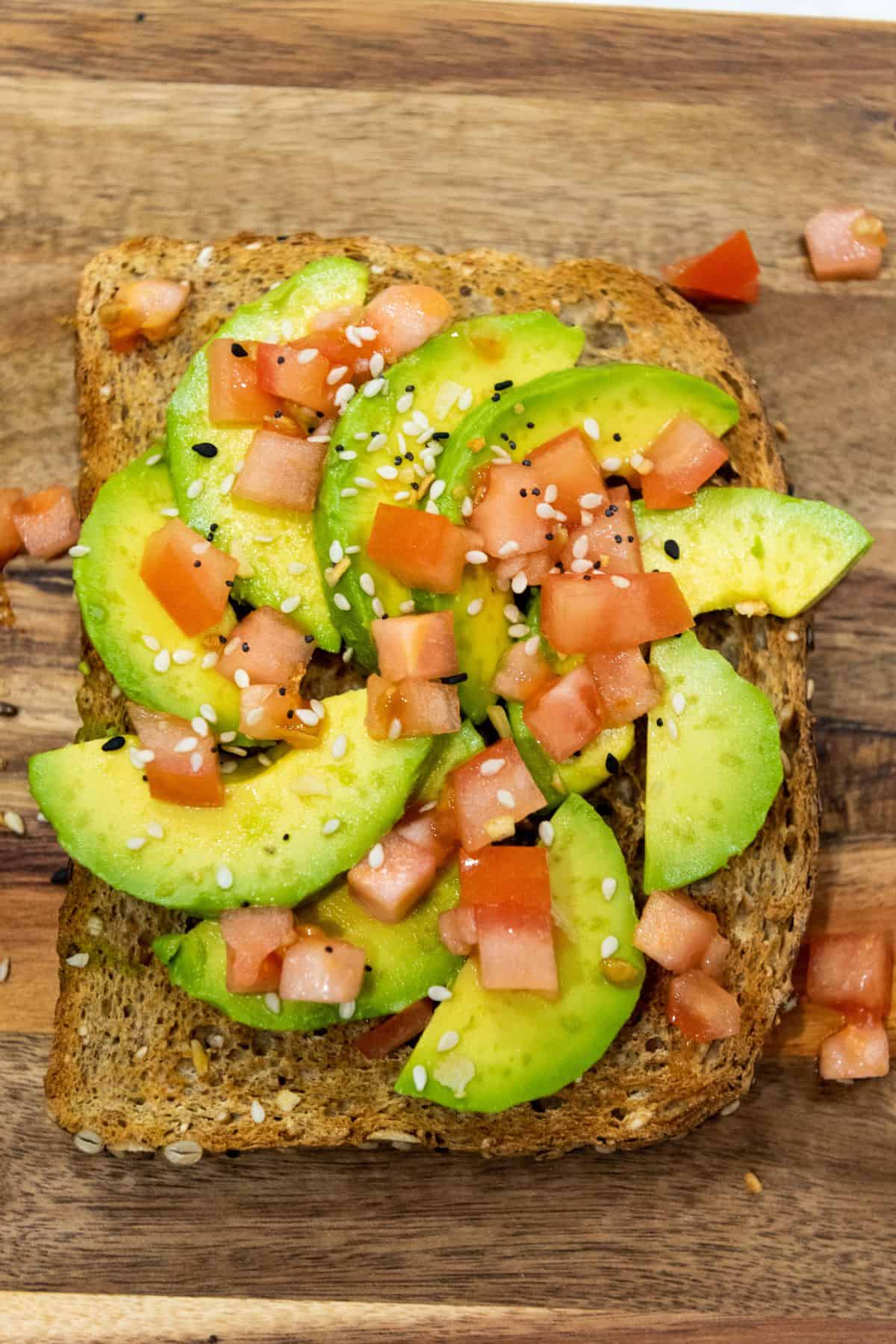 Avocado toast with sliced avocado, diced tomato, and seasoning on toasted bread.