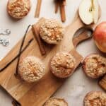 Freshly baked apple cinnamon muffins with a crumb topping, arranged on a wooden board.