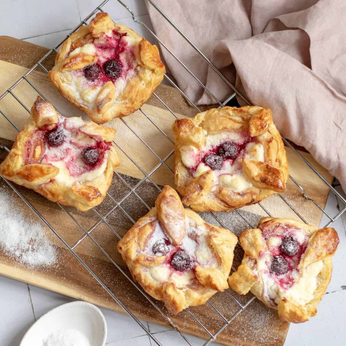 Golden-brown cherry cream cheese pastries cooling on a tray, dusted with powdered sugar.