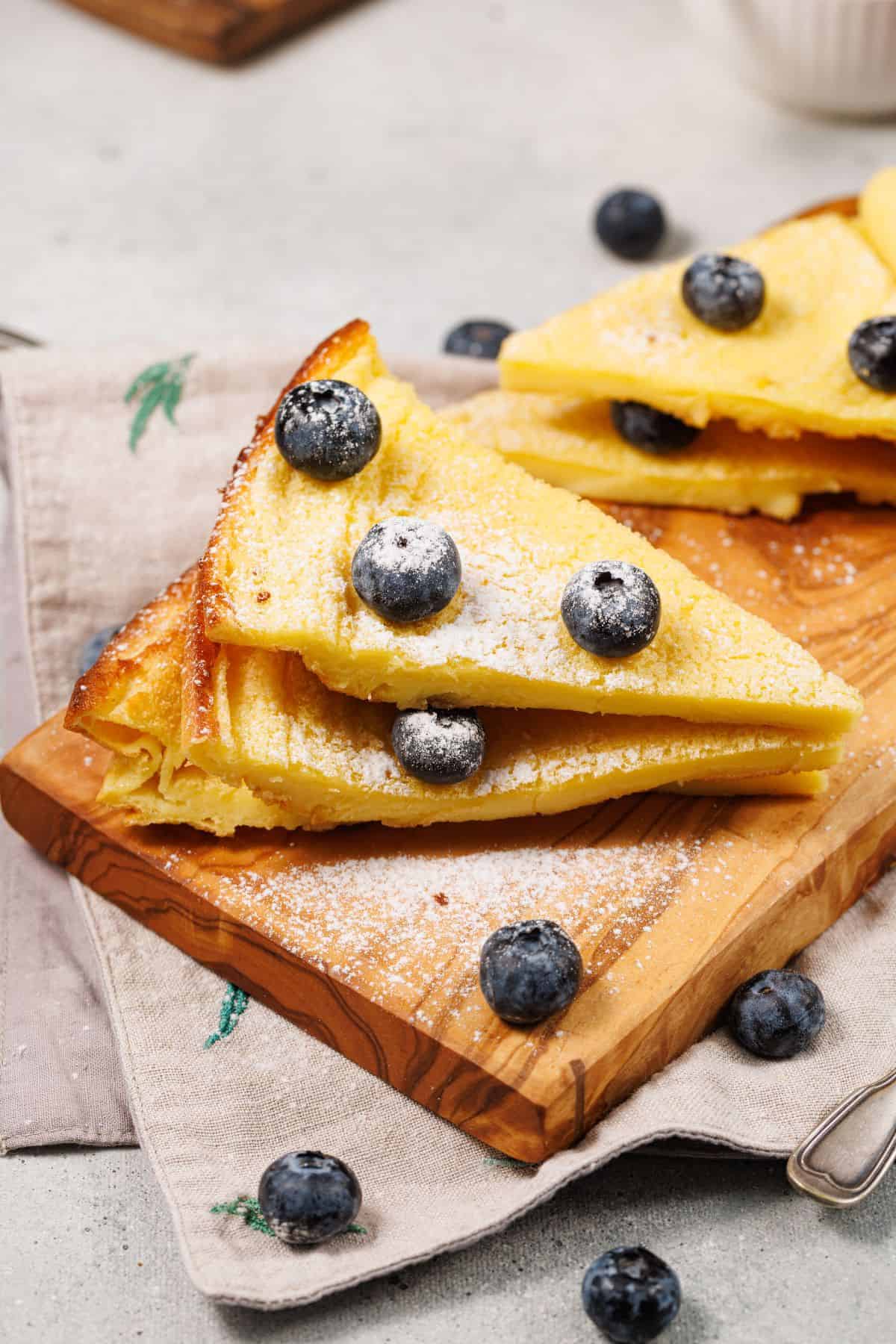 Sliced Dutch Baby pancake stacked layers, topped with powdered sugar, and surrounded by blueberries.