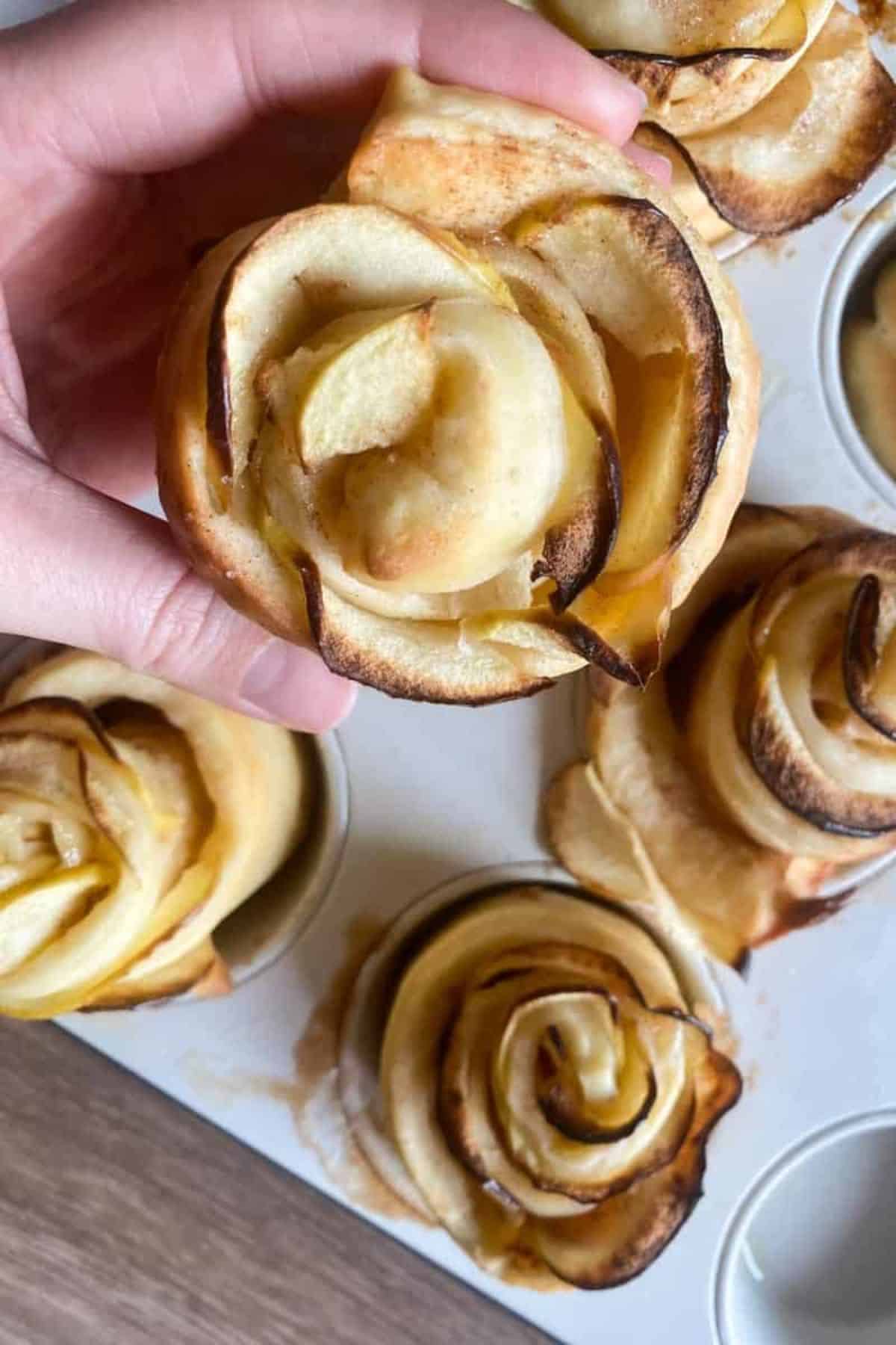 A hand holding a freshly baked sourdough apple cinnamon roll rose.
