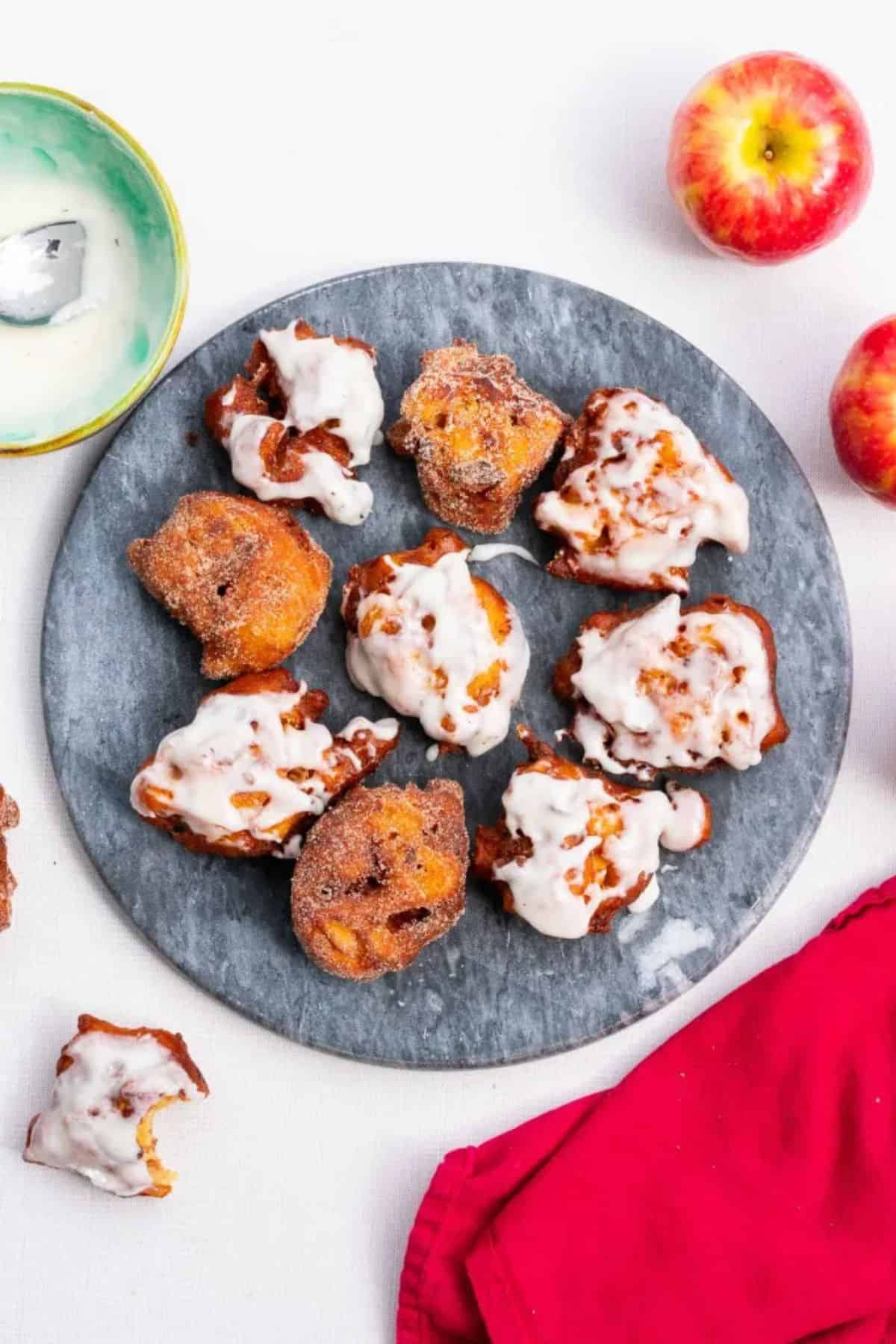 A plate of golden sourdough apple fritters—some coated in white icing, others sprinkled with sugar.