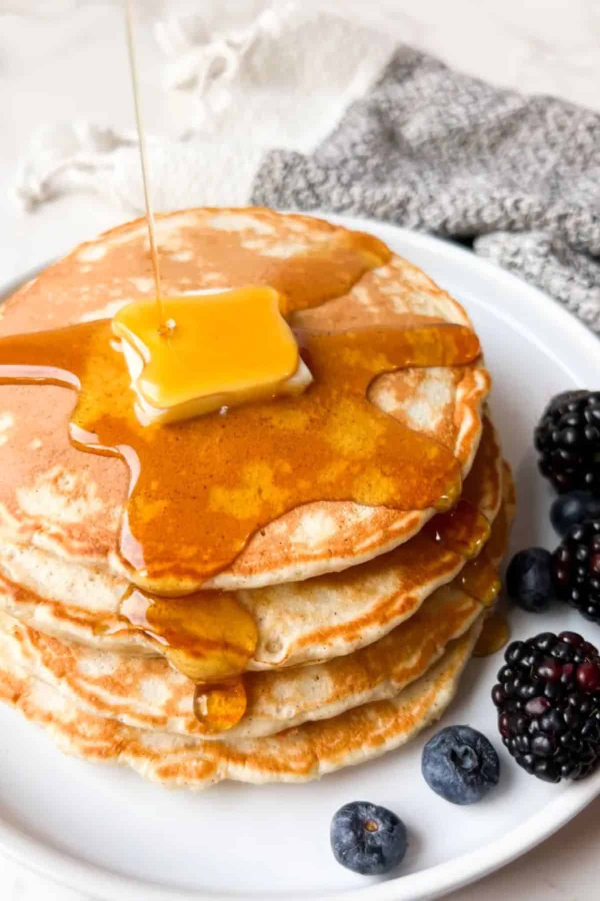 A stack of sourdough pancakes drizzled with honey, served with fresh blueberries on the side.