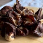 A plate with stuffed dates filled with peanut butter and coated in chocolate, with a few cut open to reveal the creamy filling.