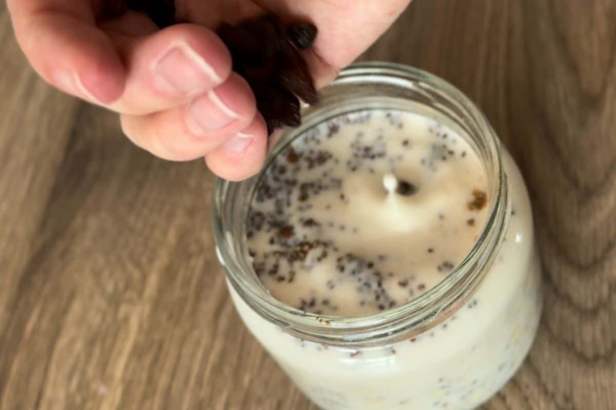 A person pouring dried fruits, like raisins and cranberries, into a jar of overnight oats.