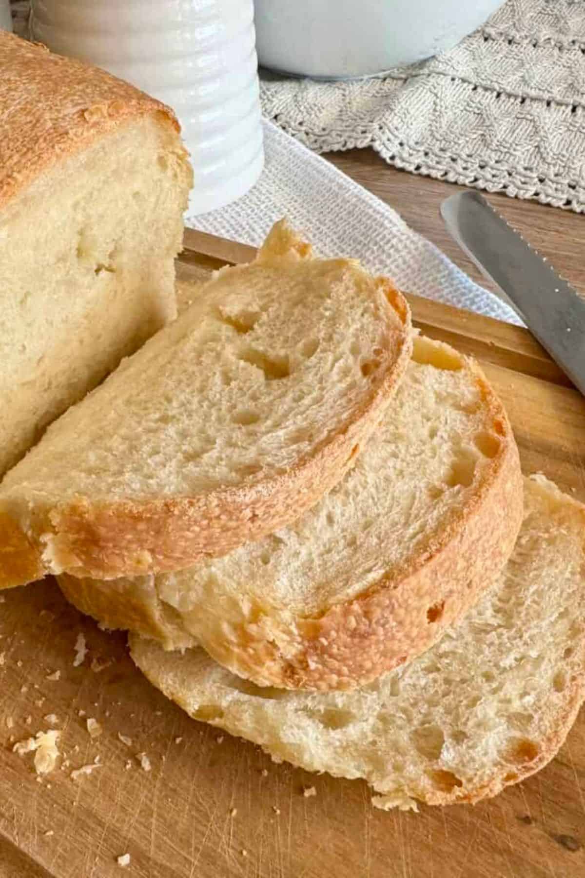A sourdough loaf with a few slices cut and arranged on a wooden board, showing the crusty exterior and soft, airy interior.