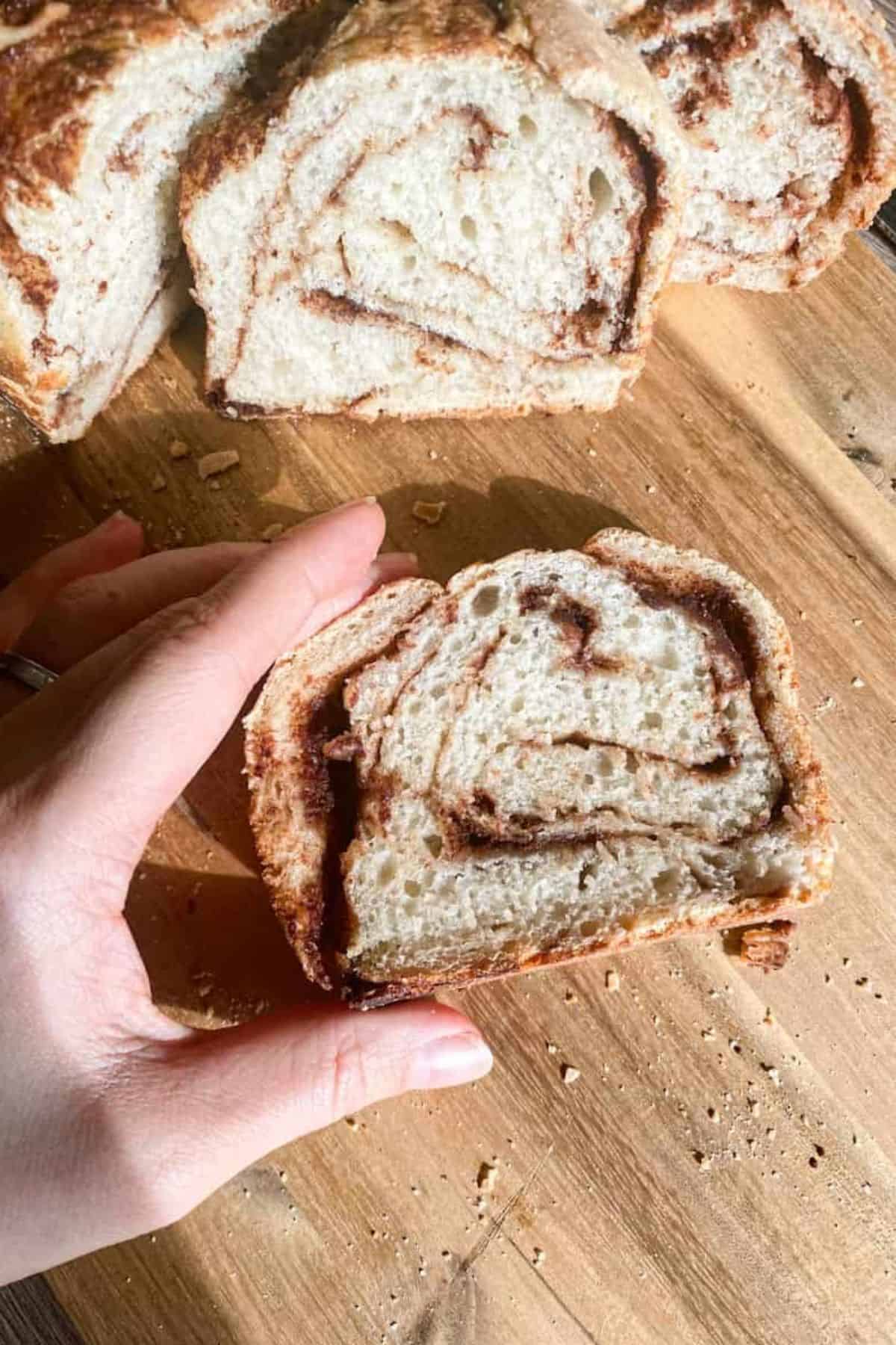 Hand holding a single sliced loaf placed on a wooden board, showing the texture of the crumb.