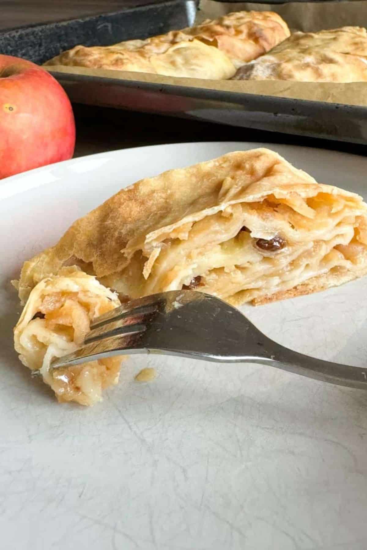 Apple strudel sliced open to show the filling, with a fork placed beside it.