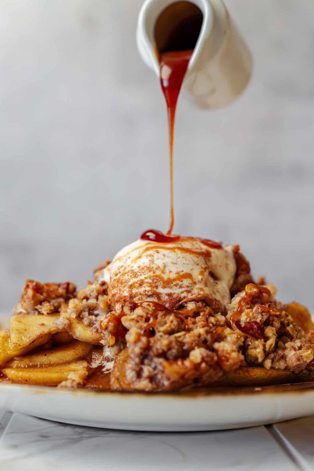 Apple crisp topped with vanilla ice cream and drizzled with syrup.
