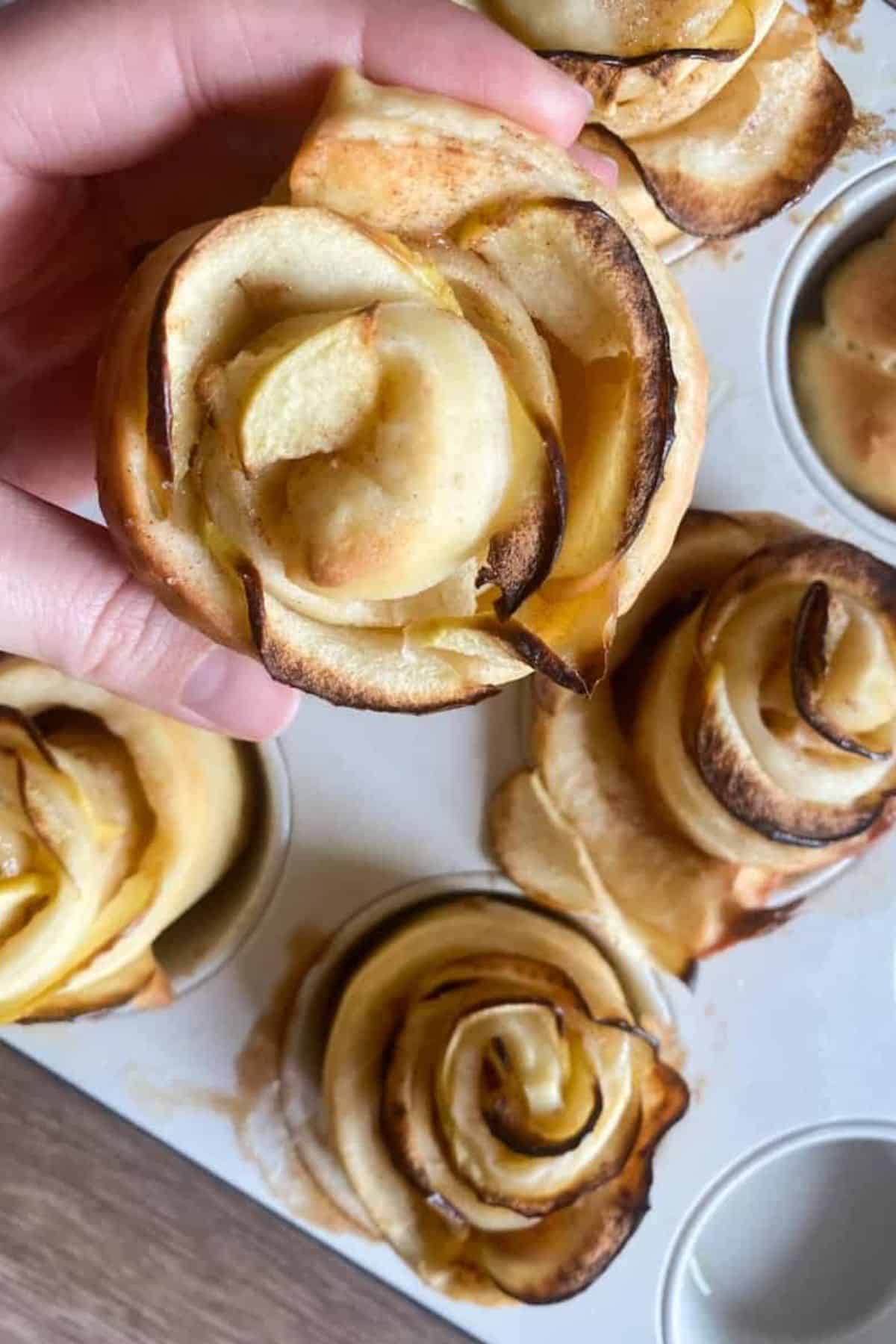 A hand holding a pastry apple rose with several more apple roses arranged in the background.