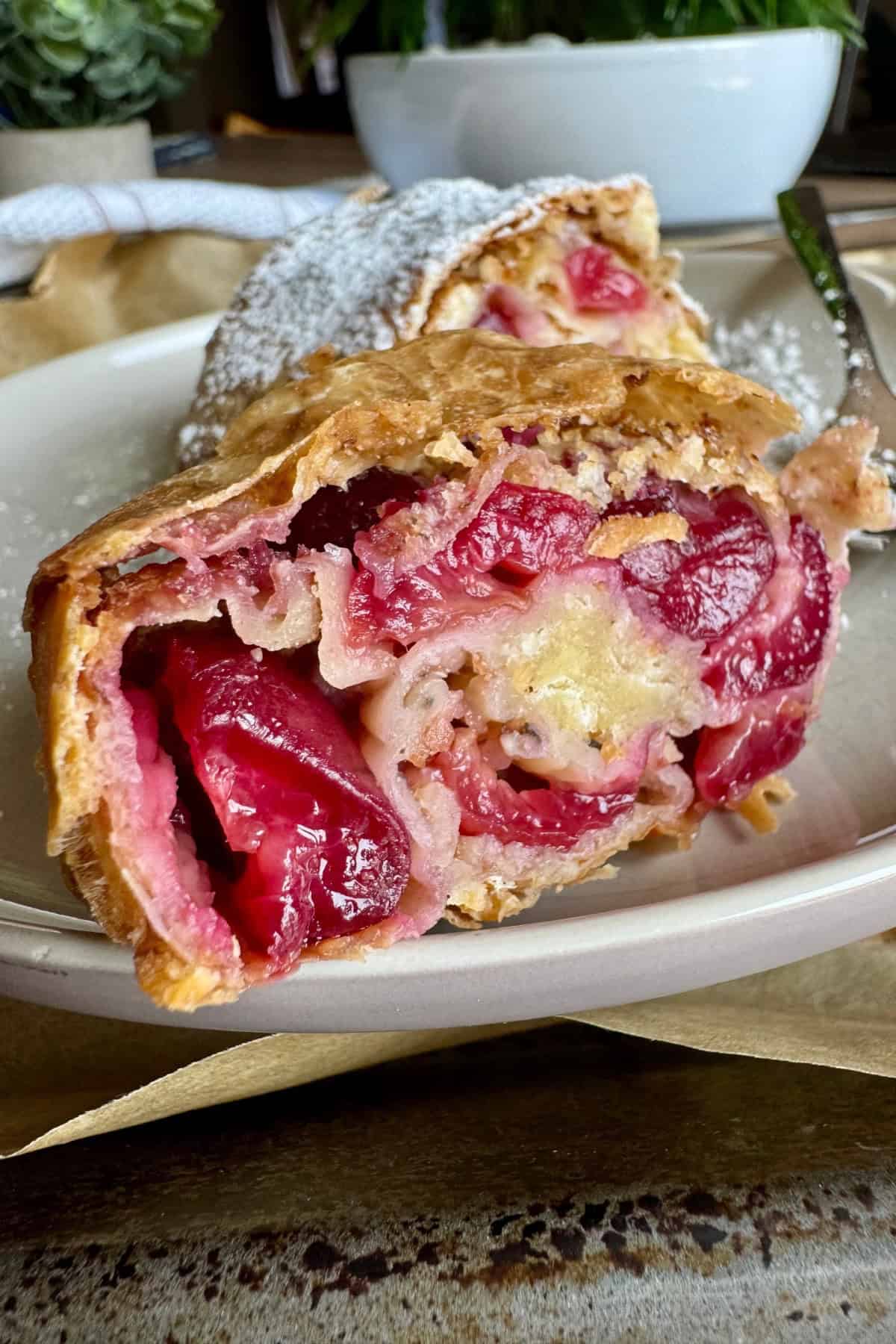 A slice of cherry strudel served on a plate, showing the interior layers of cherries, breadcrumbs, and flaky pastry.