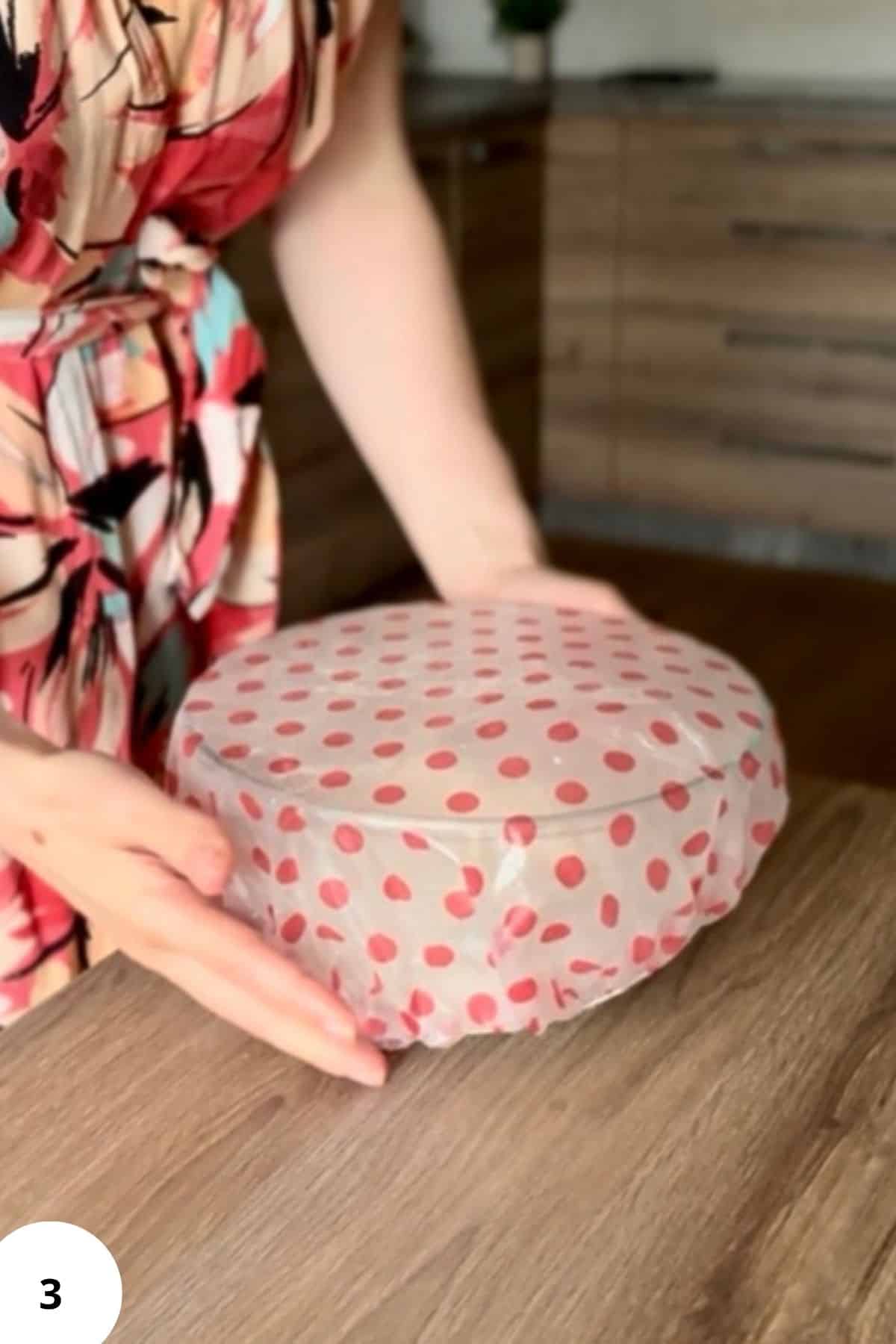 A person covering a mixing bowl of strudel dough with a plastic to let it rest.