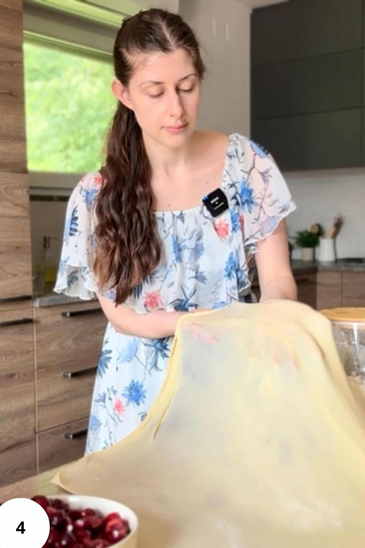 A person gently stretching flattened strudel dough by hand on a floured surface until thin.
