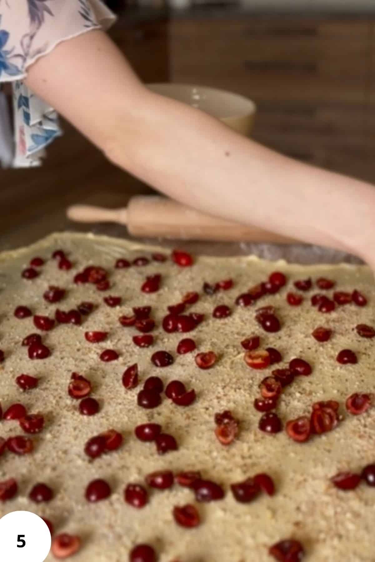 A person evenly spreading halved cherries over the stretched strudel dough.