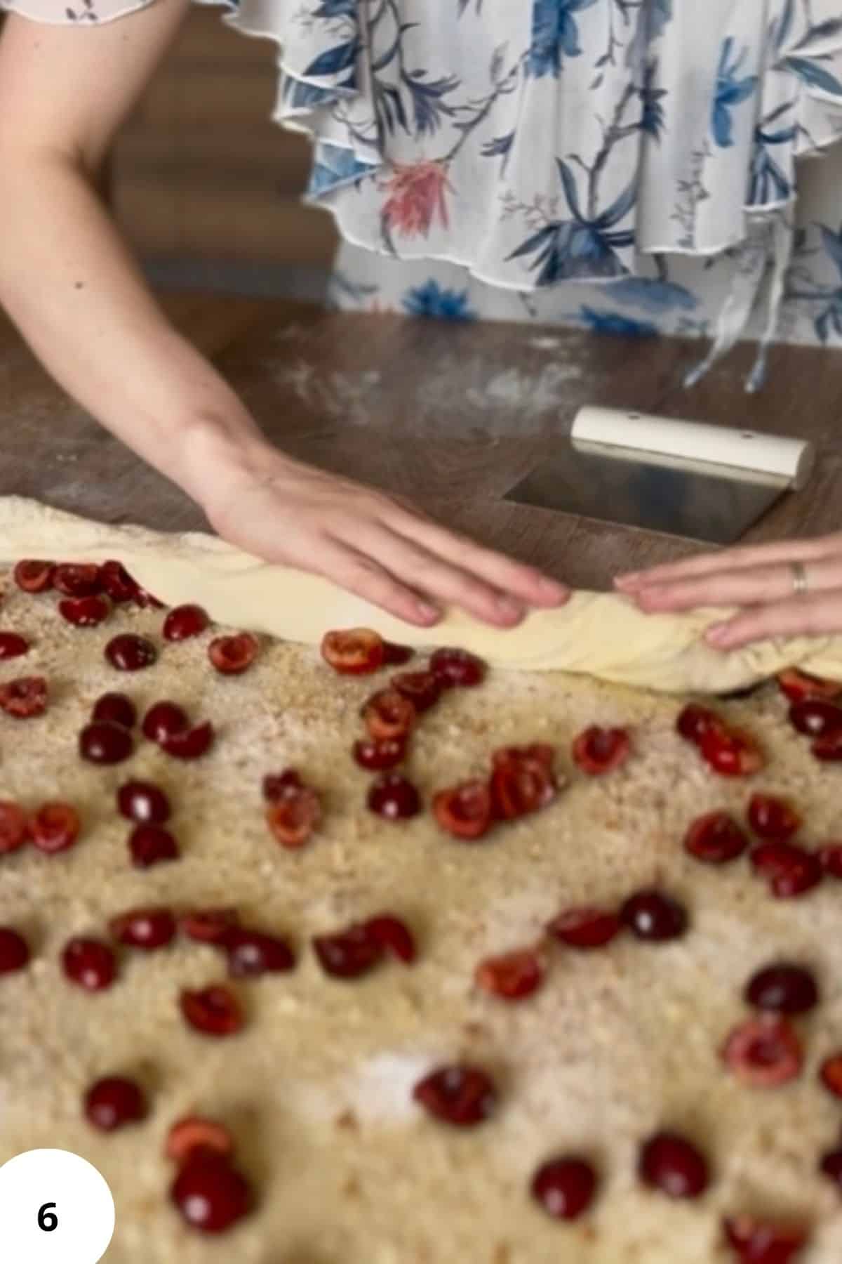 A person rolling up the filled strudel dough into a log on a floured surface.