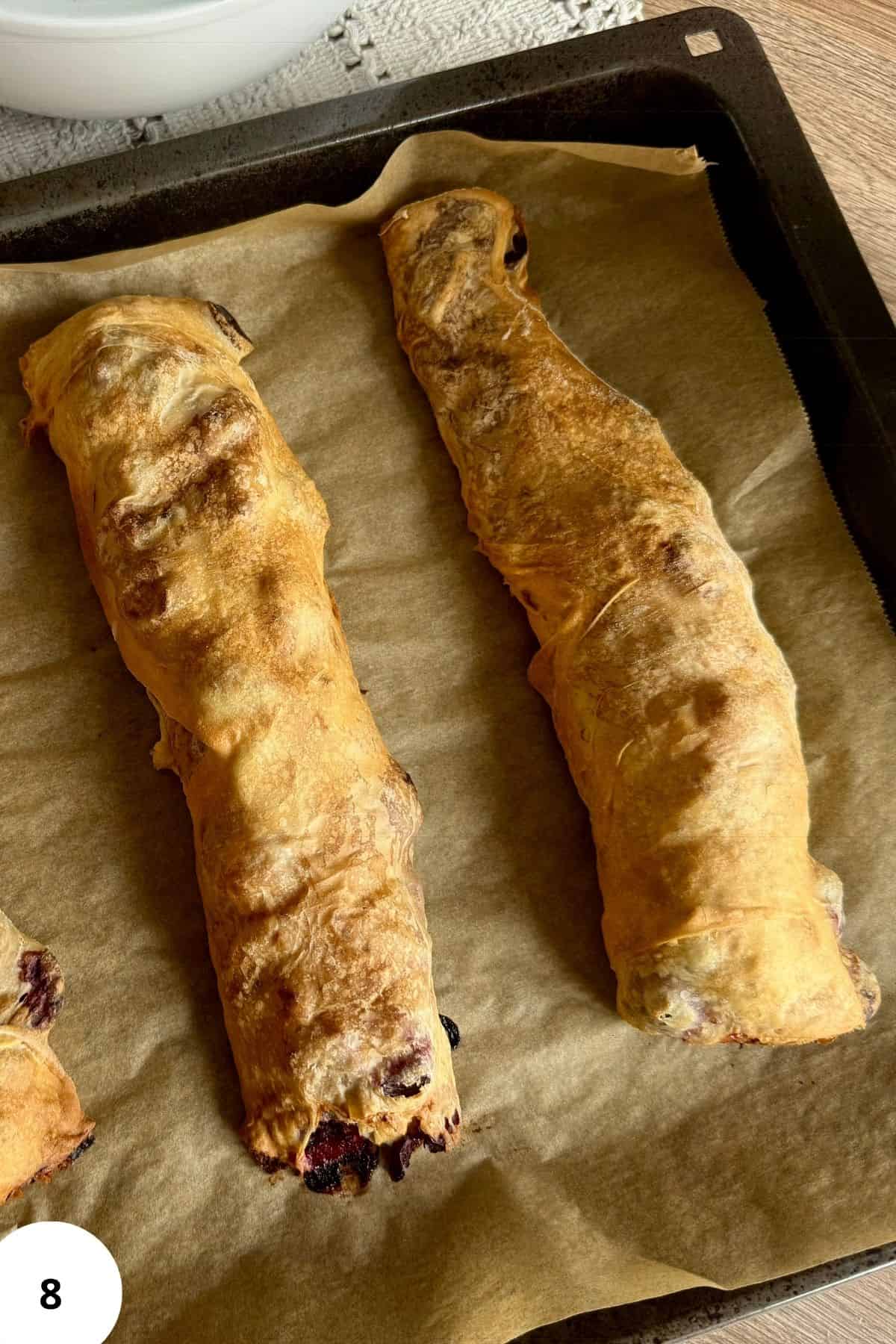 Golden-brown baked cherry strudels resting on parchment paper straight from the oven.
